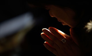 A woman is holding her hands together while praying to God in a dark room