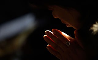 A woman is holding her hands together while praying to a God in a dark room