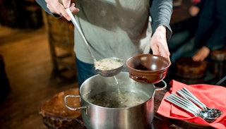 A volunteer pouring soup in a brown bowl with a metal ladle at the Food Pantry