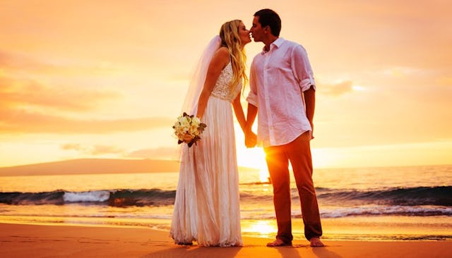 Newlywed husband and wife, sharing a romantic kiss by the sea as the sun sets.