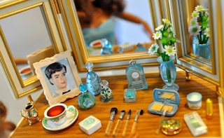 A doll makeup table with various miniature beauty products including makeup, perfume bottles and bru...