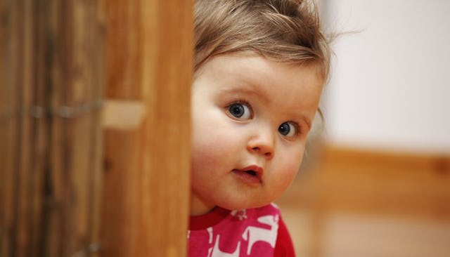 A toddler in a red-white shirt peeking behind a wooden door