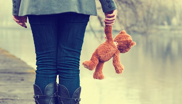 Woman standing with a teddy bear next to a river as she experiences the void as she's done having ch...