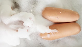 Woman covered in the foam enjoying her bath with her legs above the foam