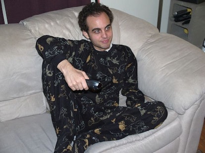 A man sitting on a white couch while wearing kids' pajamas in black with dinosaur print