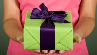 A woman wearing a pink dress handing over a present in a green packaging