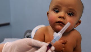 A doctor preparing a flu vaccine injection next to a baby