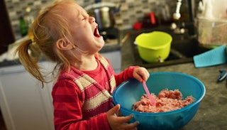 A girl is hysterically crying while trying to mix a pot with meat whose parent is experiencing wound...