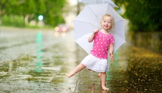 A barefoot blonde girl in a white and pink polka dot shirt and a white skirt holding a big white umb...