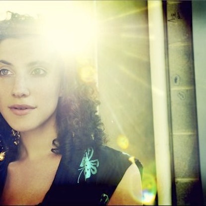 A photo by Shervin Lainez of a brunette curly-haired woman in a navy top with sunlight behind her