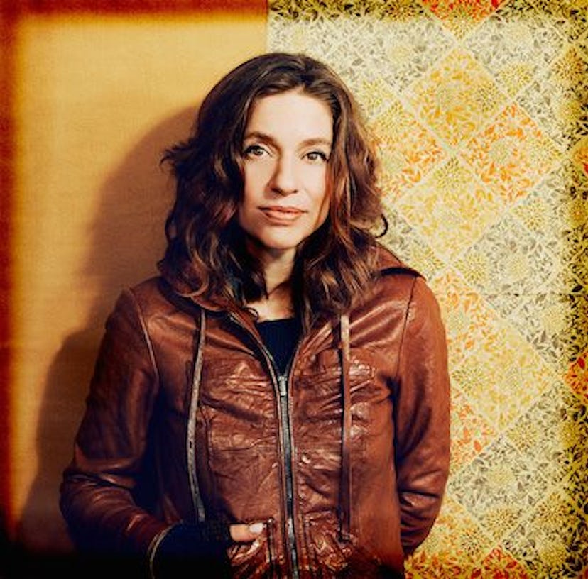 Ani DiFranco in a brown leather jacket with her hands behind her back smiling