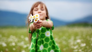 A girl in a green dress standing in a field and holding flowers