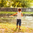A small boy standing in a white undershirt and denim shorts next to a small river