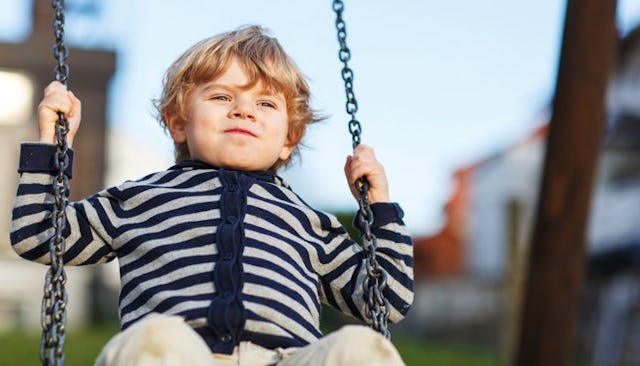 A small young boy swinging on a swing no the playground