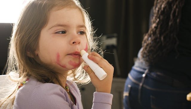 A little girl smearing red lipstick all over her face