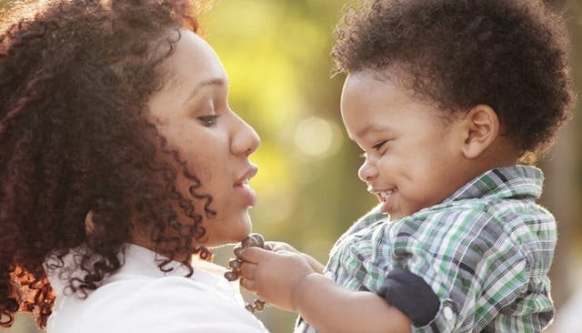 A woman holding up her toddler and both of them are smiling.