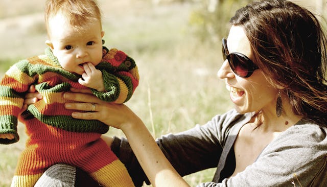 A mom holding her baby while sitting on the ground on a sunny day