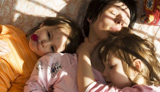 Two kids with one lying beside her mother as a part of her morning routine