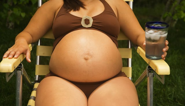 Pregnant woman sitting on a chair with a glass of water in her hand dressed in a swimming suit