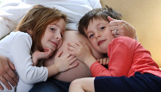 Two children leaning on their pregnant mother's belly and listening to the baby in her stomach.