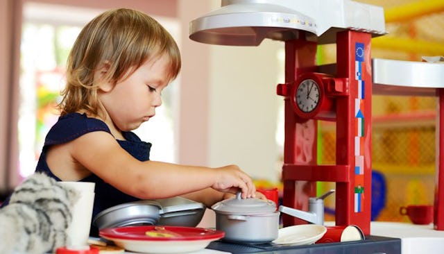 A toddler preparing a meal in her play kitchen.