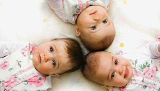 Baby triplets lying down on a bed together, head to head.