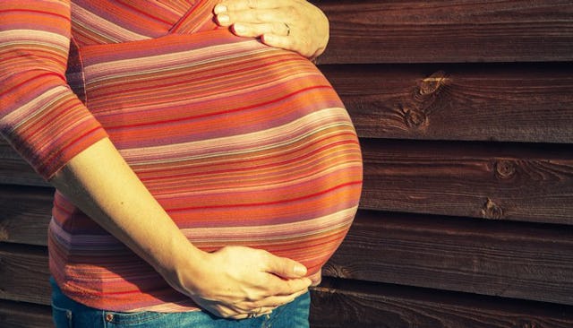 A pregnant woman in a striped orange shirt holding her belly