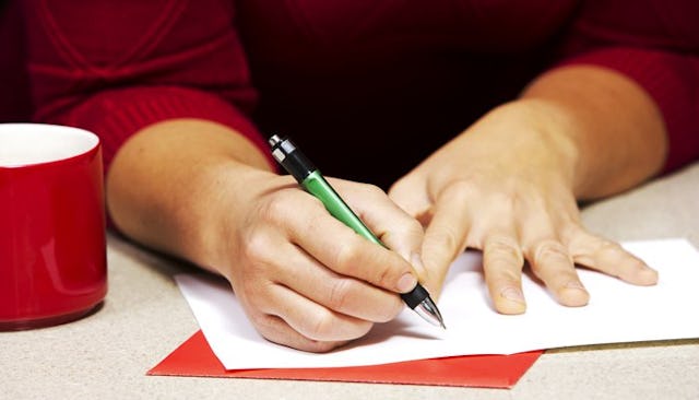A woman in a red sweater writing on a holiday card