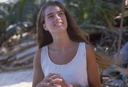 A young Brooke Shields, in a white top, smiling in nature  