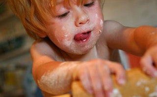 A child with short hair and bangs rolling dough for Christmas cookies with flour smeared all over it...