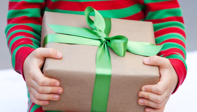 A child wearing a green-and-red striped shirt holding a gift wrapped in brown paper with a green bow...
