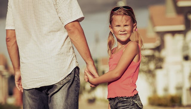 A father in a white shirt and blue jeans holding the hand of his daughter wearing pigtails, a pink t...