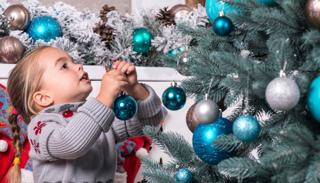 A half-Jewish child in a grey-red knit sweater hanging decorations on a Christmas tree