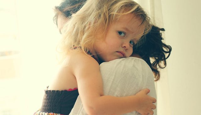 A blonde toddler being held by her mother looking over her shoulder