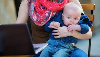 A mom going through her google search history on her laptop while holding her child 