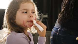 A girl applying lip balm on her upper lip while she has lipstick smeared all over her face