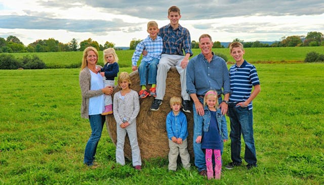 A married couple with seven children posing outside for a photo with two boys sitting on a square b...