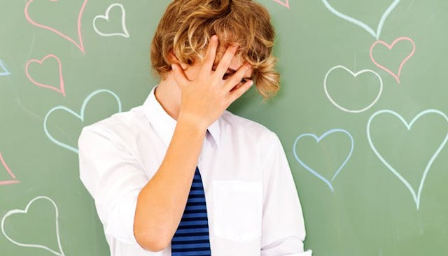 A teenager hiding his face with his hand and the chalkboard covered in hearts in the background, shy...