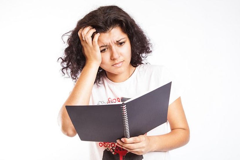 A brunette woman looking at a notebook and scratching her head from stress 