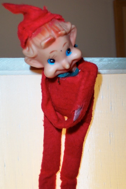 A standing red-haired elf on the shelf with blue eyes, red hair, red hat and a red romper