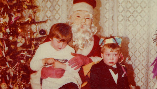 An old photo of two male kids sitting on Santa's lap beside a Christmas tree