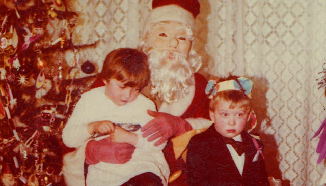 An old photo of two male kids sitting on Santa's lap beside a Christmas tree 