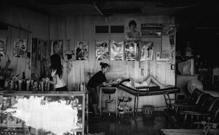 Black and white image of a hair salon, posters on walls, woman lying down while the hairstylist wash...