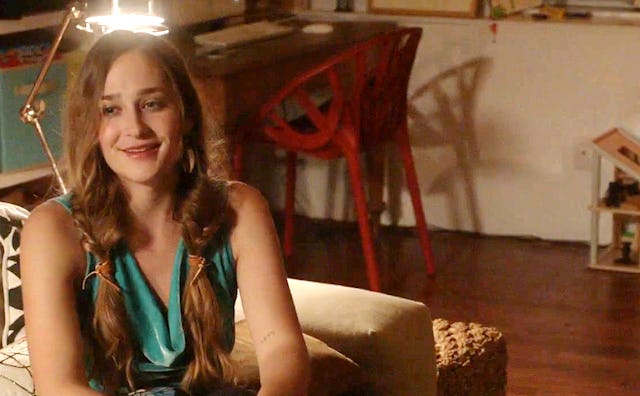 Jemima Kirke dressed up in a green blouse sitting on the couch