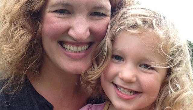 A curly-haired mother holding her daughter while they're both smiling