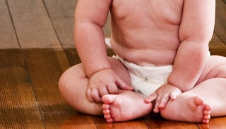 A one year old baby sitting on the floor in diapers