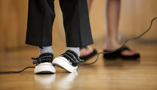 A close-up of a child standing in black pants and black and white trainers with Velcro straps on sta...