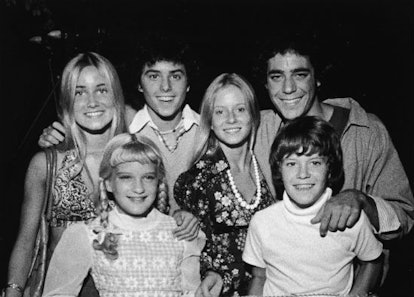 The Brady bunch cast standing together, looking straight and laughing in black and white