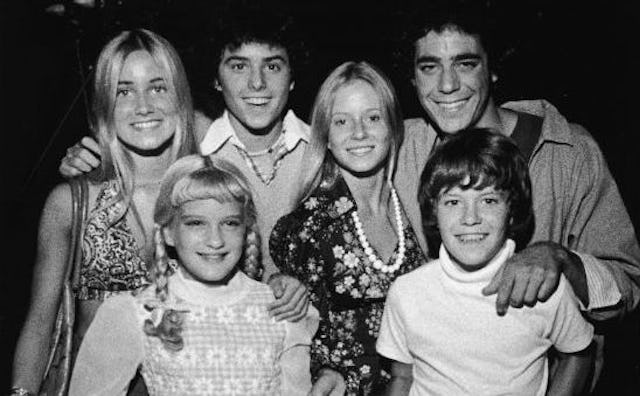 The Brady bunch cast standing together, looking straight and laughing in black and white