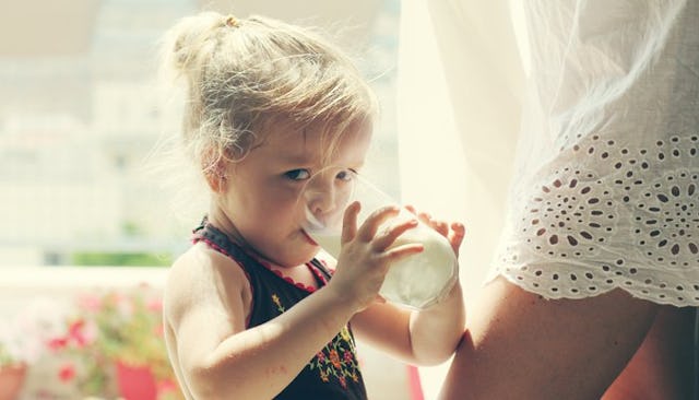 A young girl drinking milk from a glass next to her mother